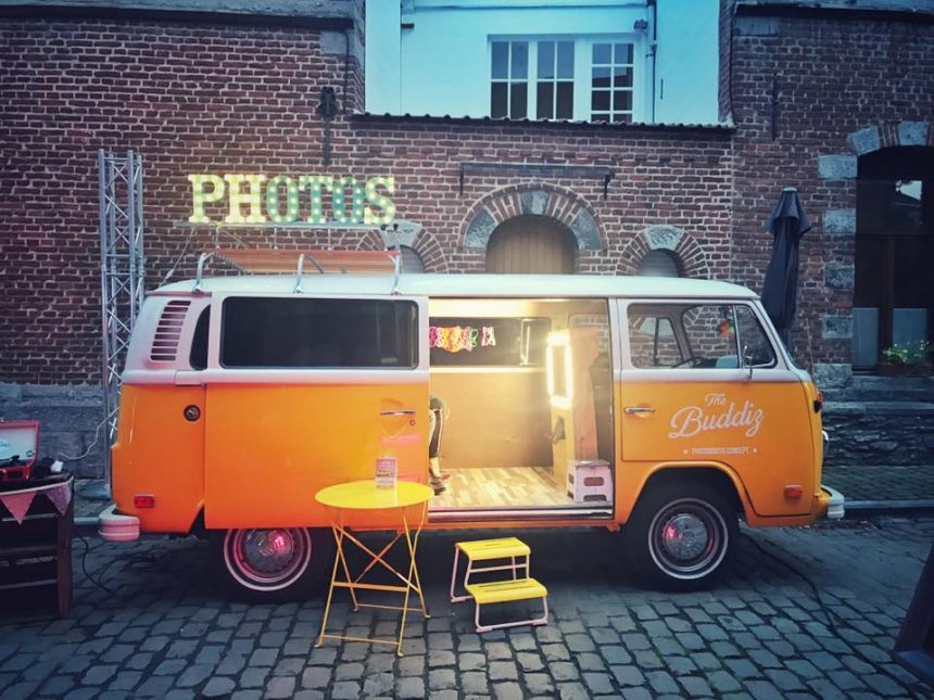 Un van avec une table et une petite marche permettant de monter dedans avec une enseigne lumineuse au dessus intitulée Photos.